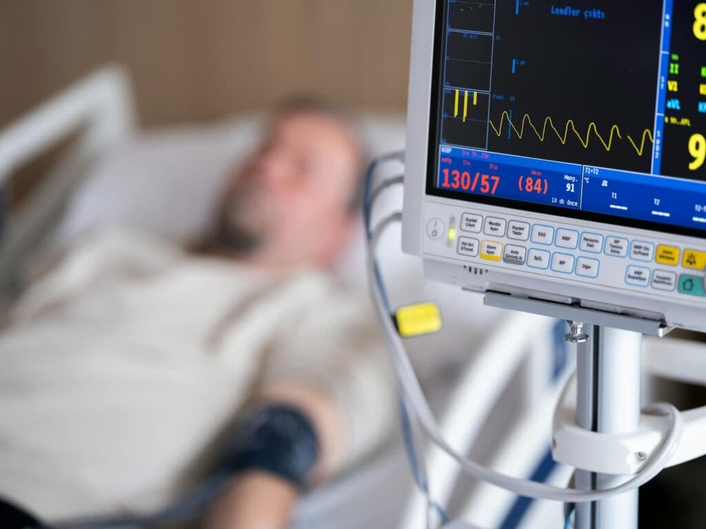 Patient in hospital bed with heart monitor showing blood pressure and heart rate.